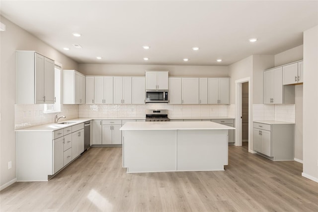 kitchen featuring decorative backsplash, a kitchen island, appliances with stainless steel finishes, light wood-type flooring, and a sink