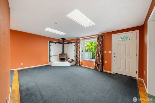 entryway with baseboards, a wood stove, and a skylight