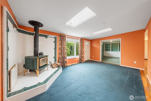 unfurnished living room with carpet flooring, baseboards, vaulted ceiling, and a wood stove