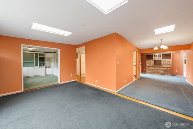 carpeted empty room with a skylight, baseboards, and a chandelier