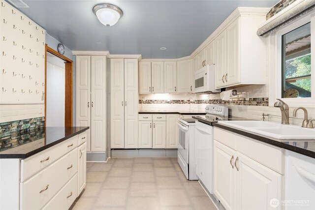 kitchen with white cabinets, dark countertops, a sink, white appliances, and decorative backsplash