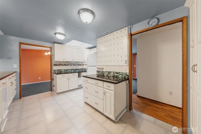 kitchen featuring dark countertops, backsplash, white cabinetry, and visible vents