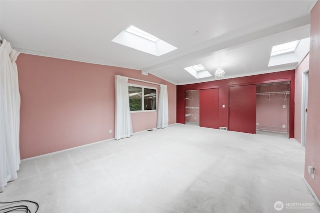 interior space featuring vaulted ceiling with skylight, baseboards, and light carpet