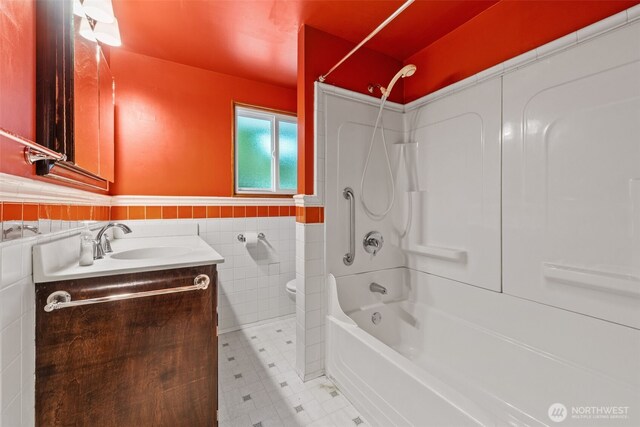 full bathroom featuring washtub / shower combination, vanity, toilet, a wainscoted wall, and tile walls