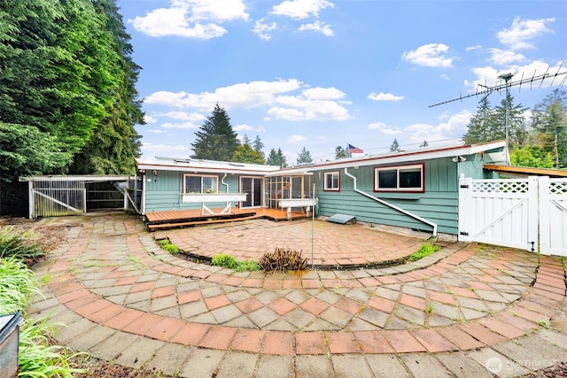 back of property featuring a wooden deck, a gate, a sunroom, fence, and a patio