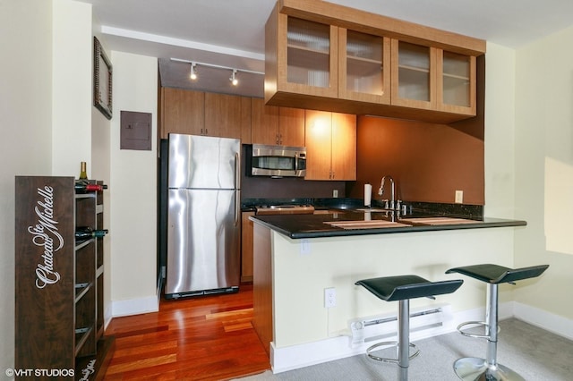 kitchen featuring brown cabinetry, dark countertops, baseboard heating, a peninsula, and stainless steel appliances