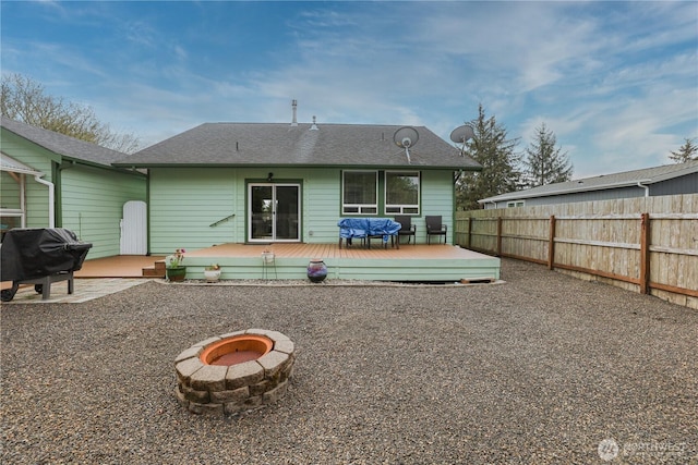 rear view of property featuring a shingled roof, an outdoor fire pit, fence, and a wooden deck