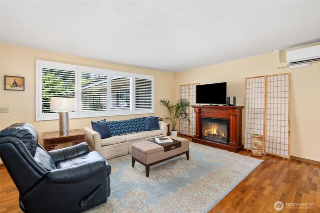 living room with an AC wall unit, baseboards, a glass covered fireplace, and wood finished floors