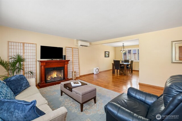 living room with a notable chandelier, a glass covered fireplace, baseboards, a wall unit AC, and wood finished floors