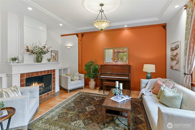 living room featuring ornamental molding, wood finished floors, recessed lighting, a textured ceiling, and a tiled fireplace