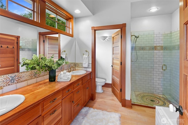 bathroom featuring double vanity, wood finished floors, toilet, a sink, and a stall shower