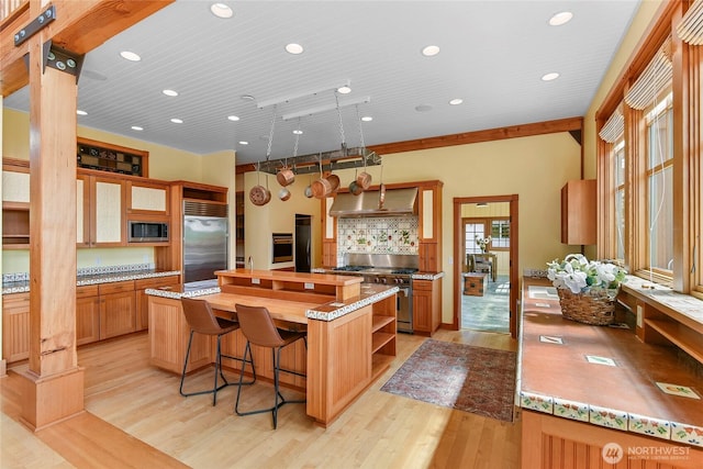 kitchen featuring open shelves, built in appliances, a center island, wall chimney exhaust hood, and light wood-style flooring