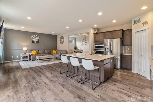 kitchen with light countertops, a kitchen breakfast bar, stainless steel appliances, open floor plan, and wood finished floors
