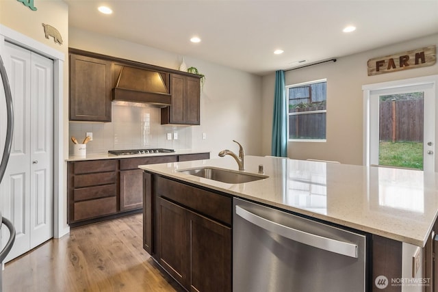 kitchen featuring an island with sink, premium range hood, light wood-type flooring, a sink, and stainless steel appliances