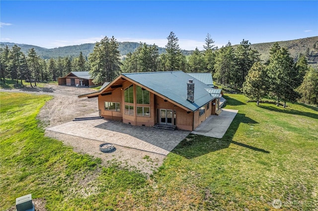 back of house featuring a yard, metal roof, driveway, and a patio