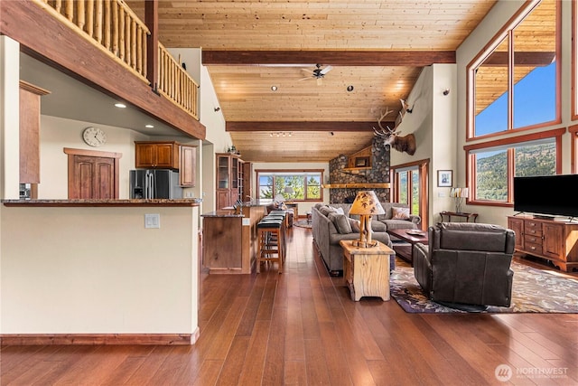 living area featuring high vaulted ceiling, dark wood finished floors, a ceiling fan, wooden ceiling with exposed beams, and baseboards
