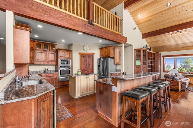 kitchen featuring stainless steel appliances, a center island with sink, a warming drawer, a sink, and dark stone counters
