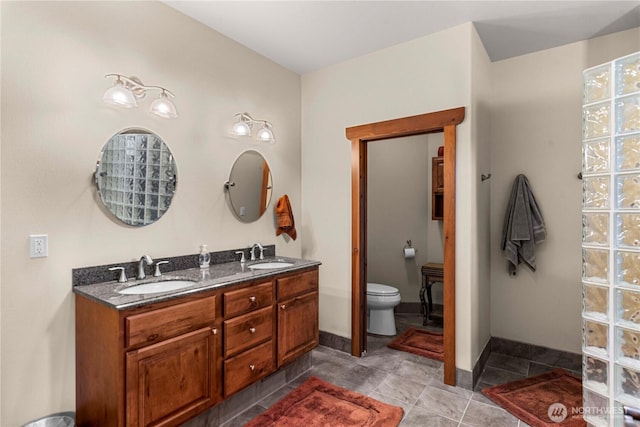bathroom with toilet, double vanity, and baseboards