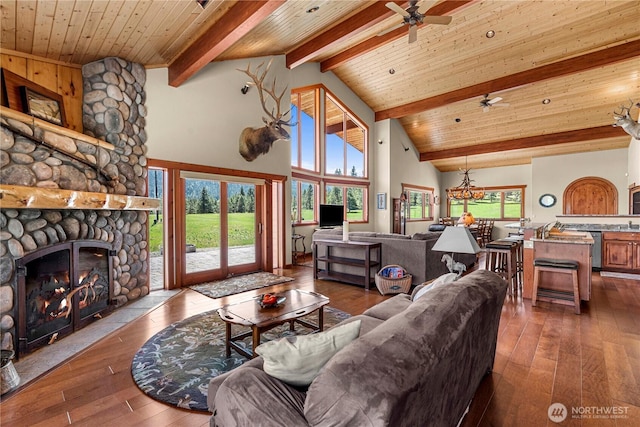 living area featuring dark wood-style floors, a stone fireplace, ceiling fan, wooden ceiling with exposed beams, and high vaulted ceiling