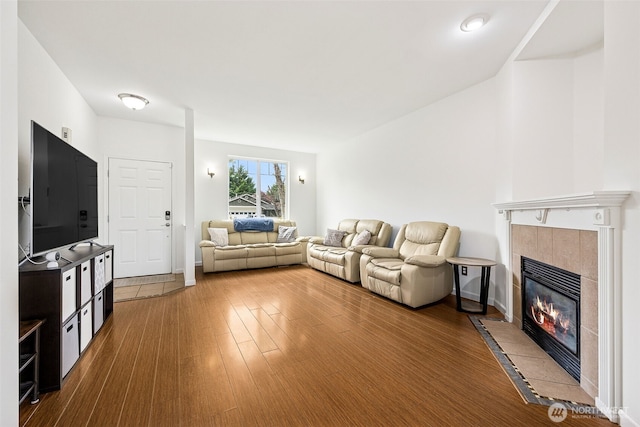 living area featuring baseboards, a tiled fireplace, and wood finished floors