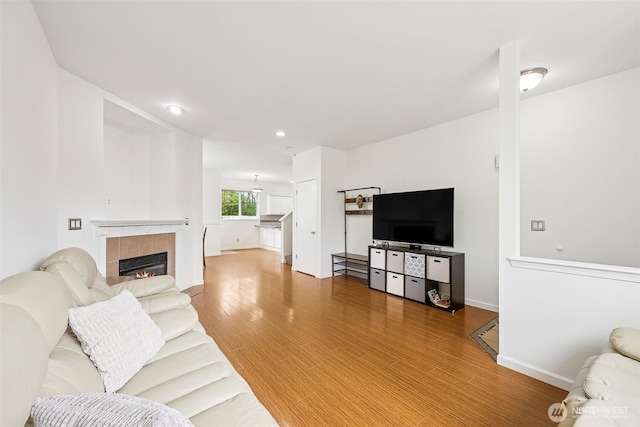 living area with recessed lighting, baseboards, a tiled fireplace, and light wood finished floors