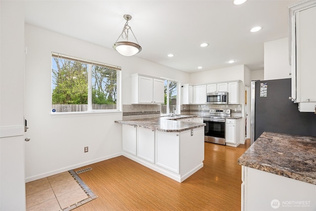 kitchen with a healthy amount of sunlight, appliances with stainless steel finishes, a peninsula, and white cabinetry