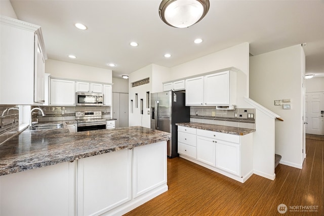 kitchen featuring appliances with stainless steel finishes, a sink, dark wood finished floors, a peninsula, and tasteful backsplash