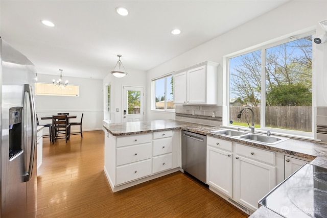 kitchen featuring a sink, a peninsula, an inviting chandelier, stainless steel appliances, and white cabinetry