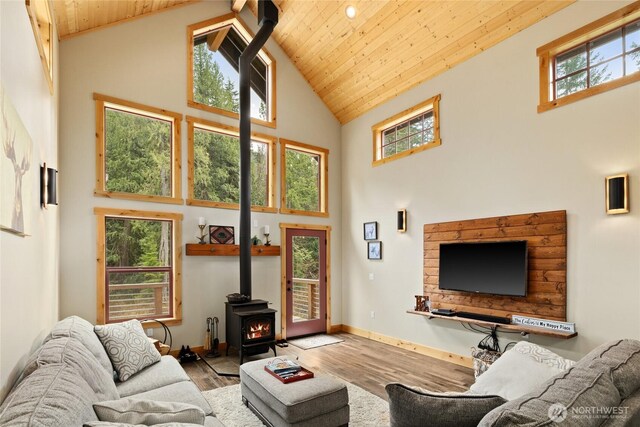 living room featuring a wood stove, wood finished floors, baseboards, high vaulted ceiling, and wood ceiling