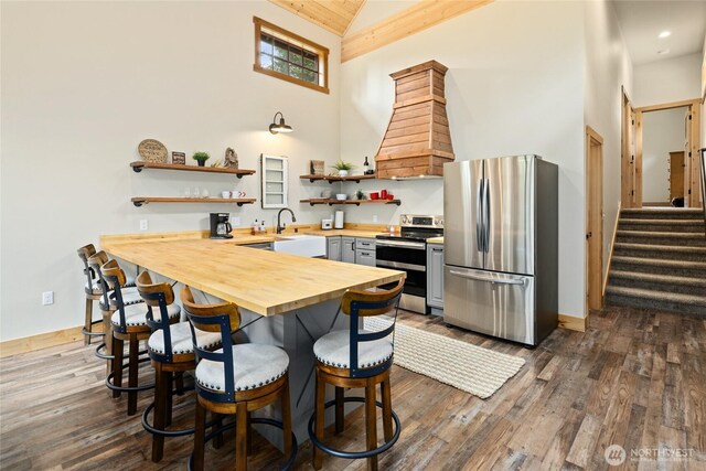 kitchen featuring open shelves, high vaulted ceiling, wooden counters, stainless steel appliances, and a kitchen bar