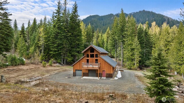 back of house featuring gravel driveway, a deck with mountain view, a wooded view, and a detached garage