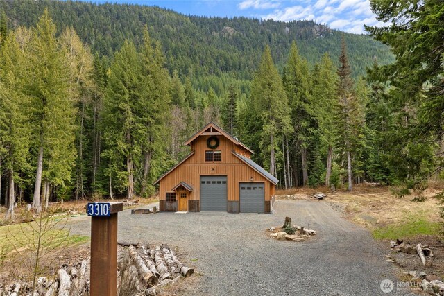 exterior space featuring a detached garage, a view of trees, driveway, and a mountain view