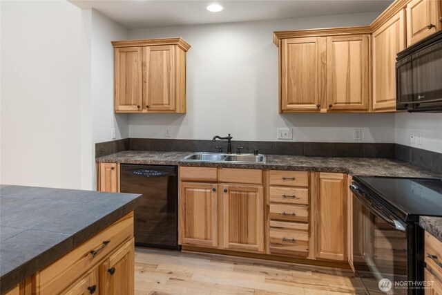 kitchen with dark countertops, a sink, black appliances, light wood-style floors, and recessed lighting