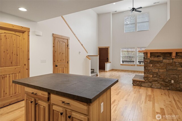 kitchen with a towering ceiling, tile counters, recessed lighting, a ceiling fan, and light wood finished floors