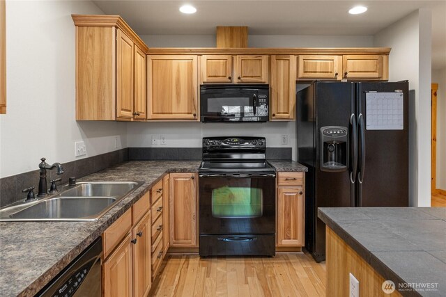 kitchen featuring dark countertops, a sink, black appliances, and light wood-style floors