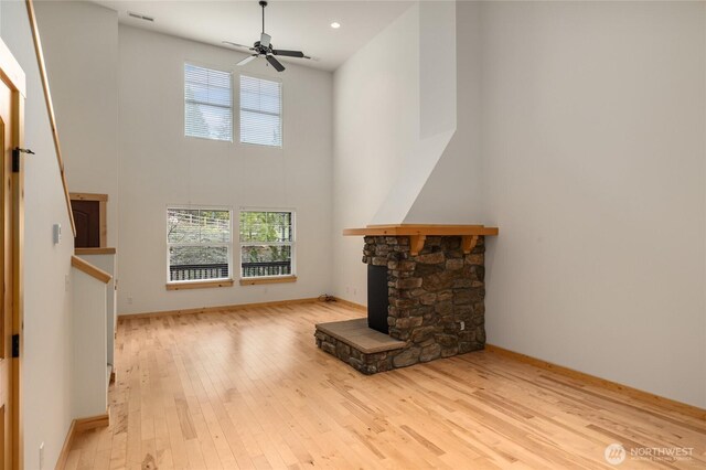 unfurnished living room featuring ceiling fan, a stone fireplace, hardwood / wood-style floors, a towering ceiling, and visible vents