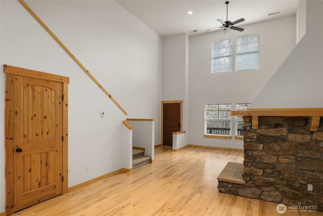 unfurnished living room featuring wood finished floors, baseboards, a high ceiling, stairway, and a ceiling fan