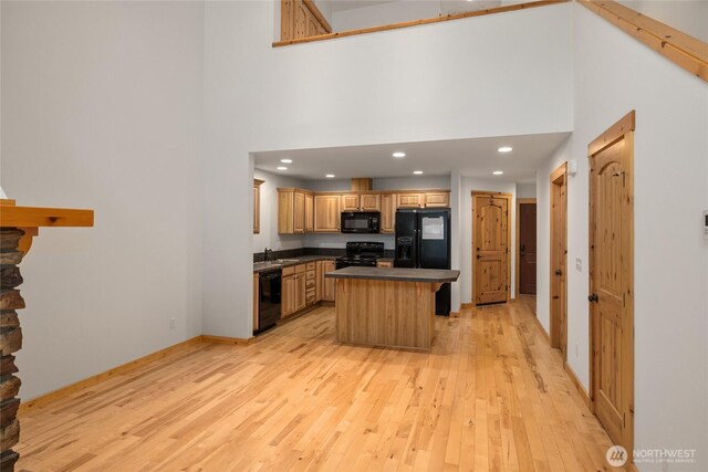 kitchen featuring dark countertops, light wood-style floors, a high ceiling, a sink, and black appliances