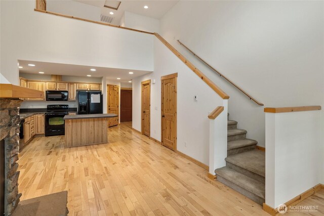 kitchen with visible vents, a kitchen island, dark countertops, light wood-style flooring, and black appliances