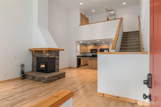 living room with a stone fireplace, stairs, recessed lighting, baseboards, and light wood-type flooring
