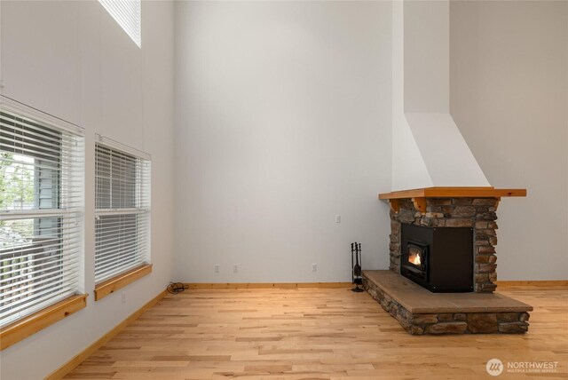 unfurnished living room with baseboards, plenty of natural light, light wood-style flooring, and a high ceiling