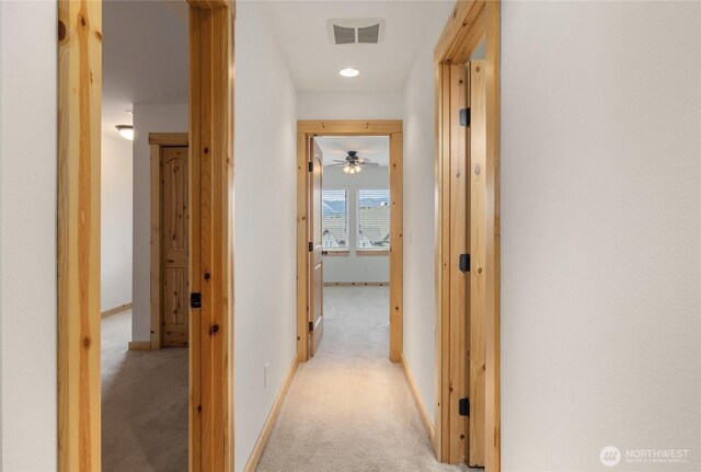 hallway featuring visible vents, baseboards, and light colored carpet