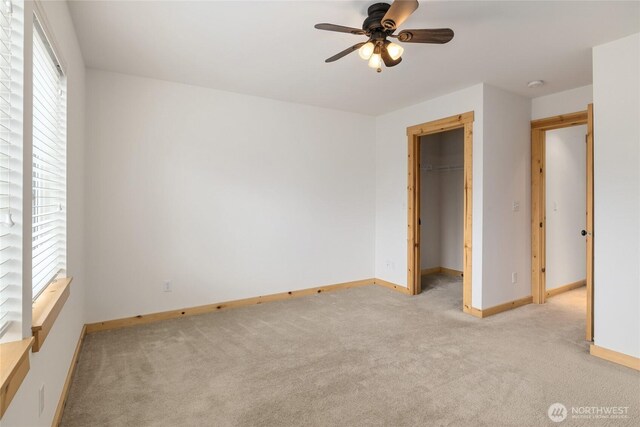 unfurnished bedroom featuring baseboards, a spacious closet, light carpet, and ceiling fan