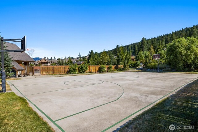 view of sport court featuring fence, community basketball court, and a forest view