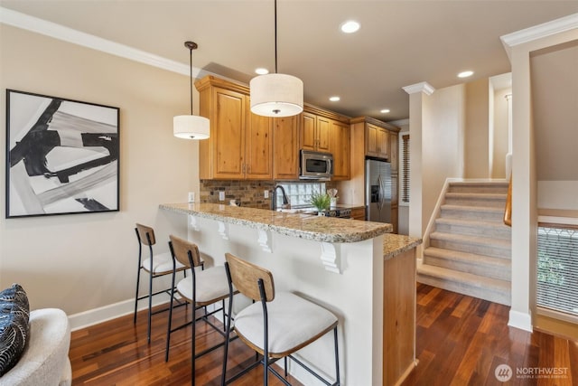 kitchen featuring ornamental molding, a breakfast bar, baseboards, dark wood finished floors, and stainless steel appliances