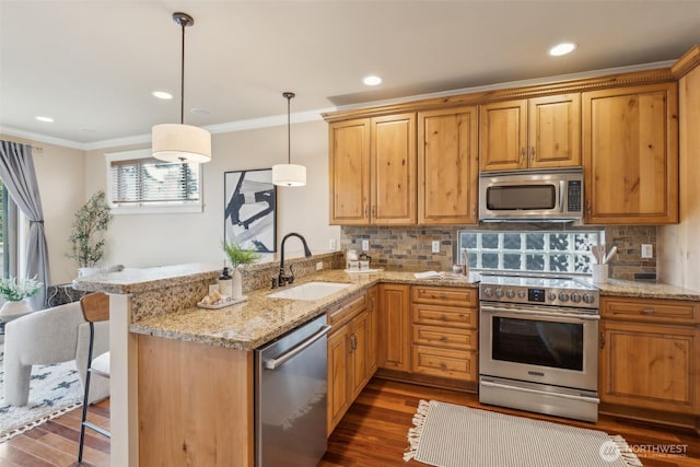 kitchen with a peninsula, appliances with stainless steel finishes, ornamental molding, and a sink