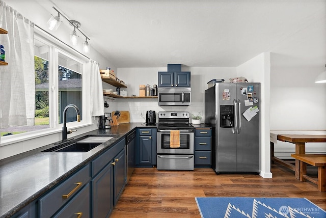 kitchen featuring open shelves, dark countertops, a sink, stainless steel appliances, and blue cabinets