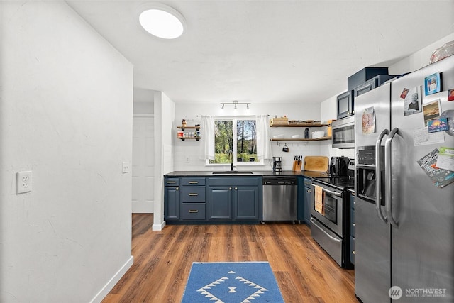 kitchen featuring open shelves, wood finished floors, dark countertops, a sink, and appliances with stainless steel finishes