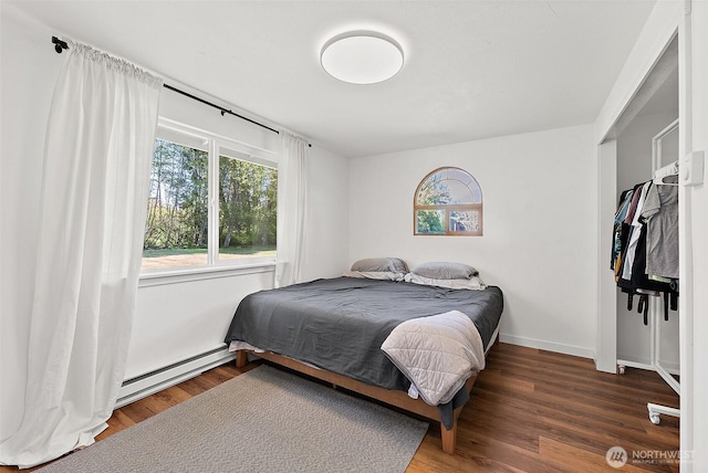 bedroom with baseboards, multiple windows, wood finished floors, and a baseboard radiator