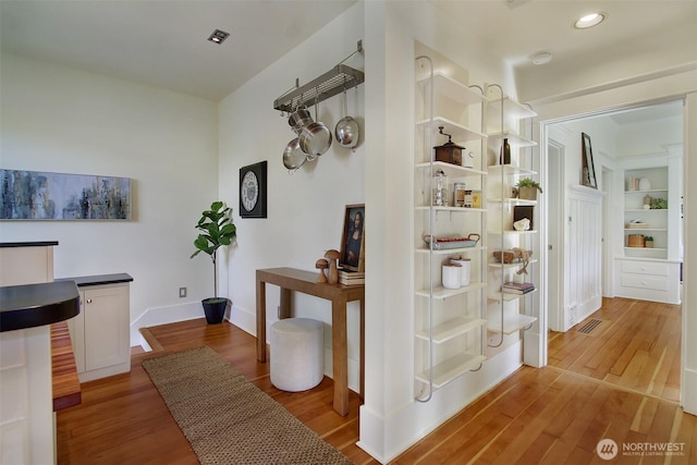 hall with baseboards, visible vents, and wood finished floors